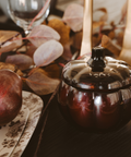 Pumpkin candle with a lid on a table with autumn leaves.