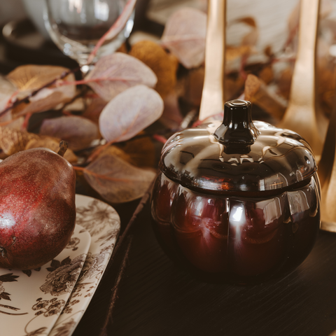 Pumpkin candle with a lid on a table with autumn leaves.