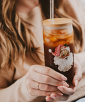 Person holding a glass tumbler with a Santa Claus design, filled with a beverage.