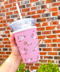 Hand holding a pink patterned cup with a straw against a brick wall.
