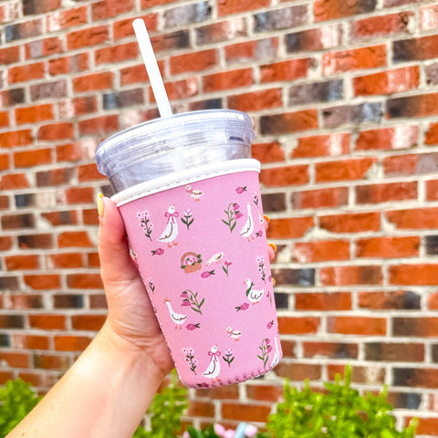 Hand holding a pink patterned cup with a straw against a brick wall.