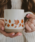 Person holding a mug with autumn leaf design