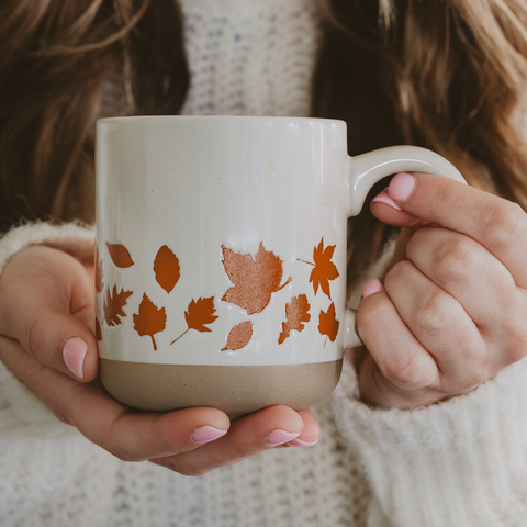 Person holding a mug with autumn leaf design