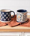 Two ceramic mugs with decorative patterns on a wooden surface.