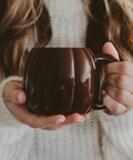 Person holding a dark brown mug with a blurred background