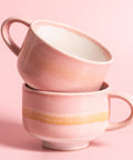 Two pink ceramic mugs stacked on a pink background