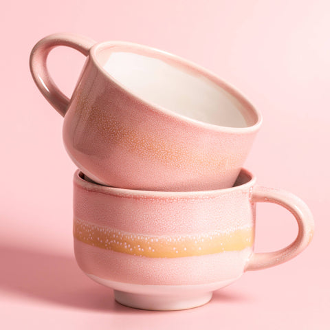 Two pink ceramic mugs stacked on a pink background