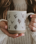Person holding a mug with leaf patterns against a neutral background