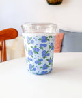 Clear glass tumbler with blue floral pattern sleeve on a white surface
