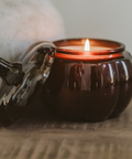 Ceramic pumpkin-shaped candle with a lit wick on a wooden surface