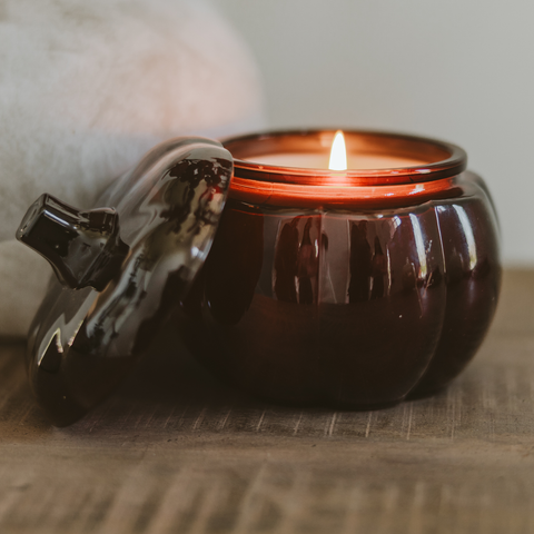 Ceramic pumpkin-shaped candle with a lit wick on a wooden surface