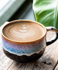 Ceramic mug with a layered design on a wooden surface with green leaves in the background
