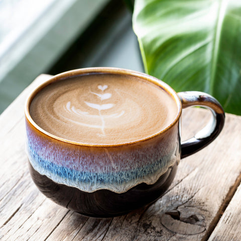 Ceramic mug with a layered design on a wooden surface with green leaves in the background