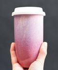 Hand holding a pink gradient tumbler against a dark background
