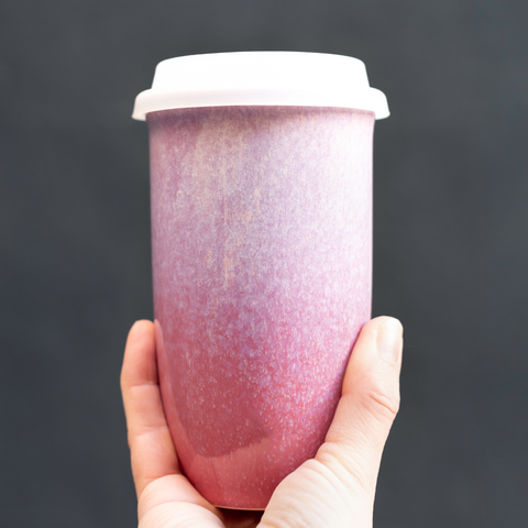 Hand holding a pink gradient tumbler against a dark background