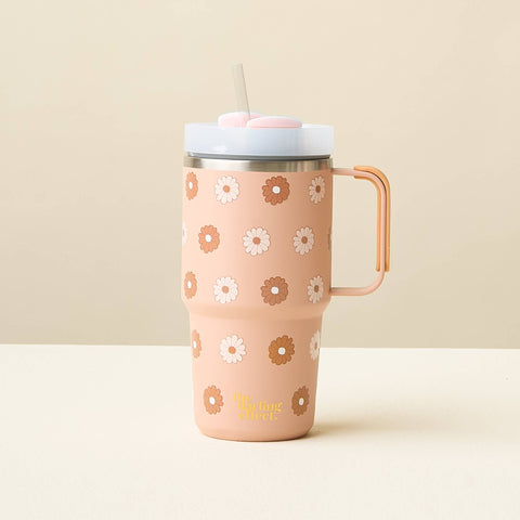 A tan-colored insulated travel tumbler with a handle, decorated with a pattern of white and brown daisies. It features a light blue lid with a clear straw, set against a minimalist beige background.
