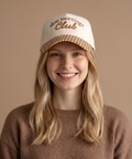 Woman wearing a cap with 'slow mornings Club' text on a beige background