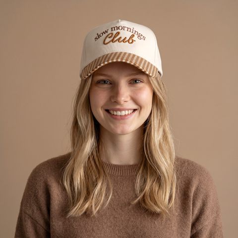 Woman wearing a cap with 'slow mornings Club' text on a beige background