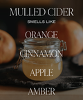 Glass jar of mulled cider with pumpkins in the background, text describing scents.